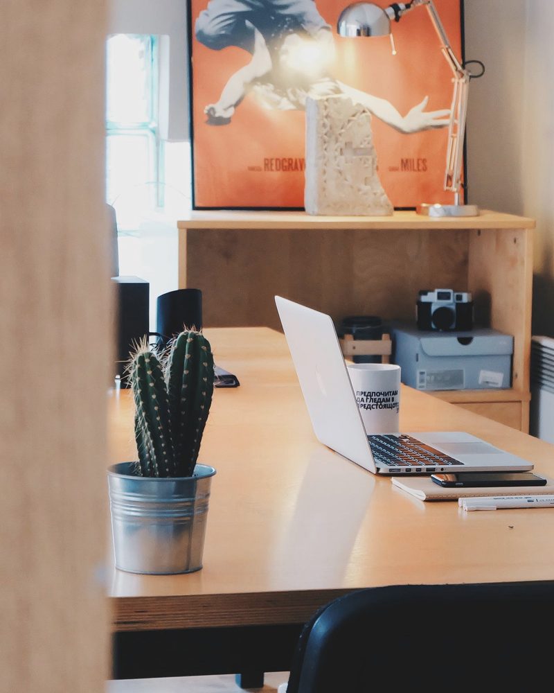 A tidy desk with an open laptop and a small plant beside a window
