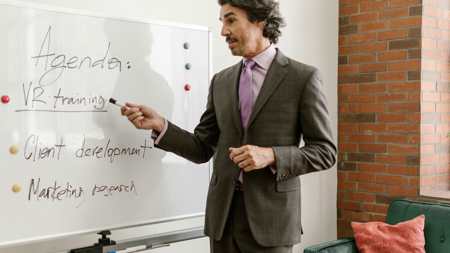 A presenter working through a written agenda on a whiteboard