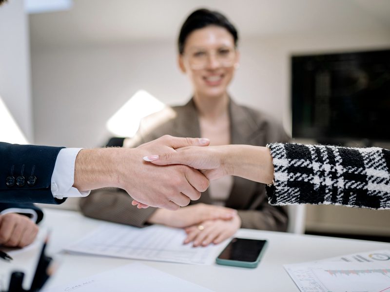 Two professionals shaking hands across a desk after a conversation